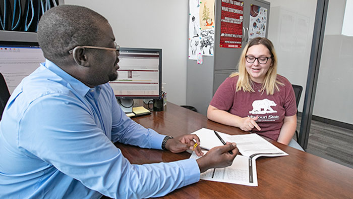 An academic advisor in the College of Business reviewing paperwork with a student. 