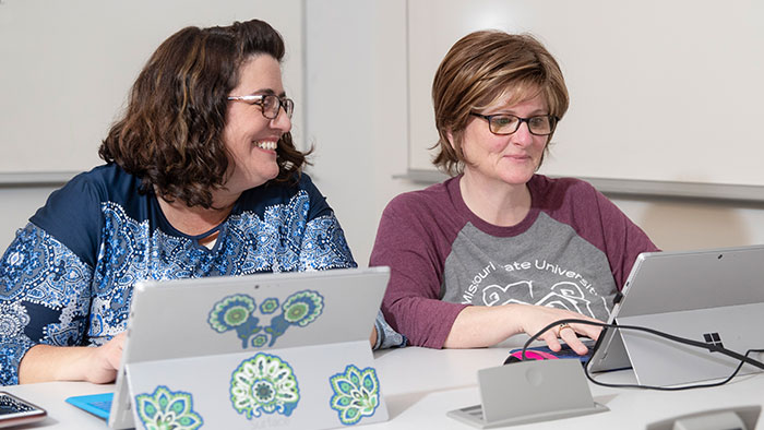 Two women working on their laptops smiling